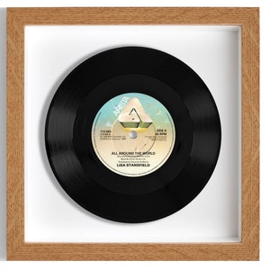 May include: A framed black vinyl record with a white label. The label has the text "Arista" and "All Around The World" by "Lisa Stansfield".