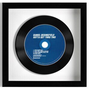 May include: A black framed picture of a CD single by Daniel Bedingfield. The CD is blue and black and has the title "Gotta Get Thru This" printed on it. The CD is surrounded by a black vinyl record.