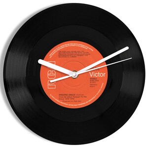 May include: A black vinyl record clock with white hands. The record label is orange and features the text "Victor" and "Amazing Grace".