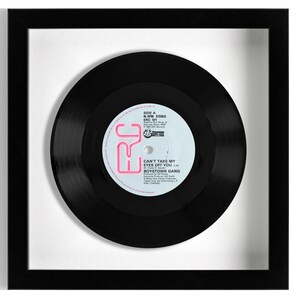 May include: A black vinyl record in a white frame. The record label is pink and white and says "Can't Take My Eyes Off You" by Boystown Gang.