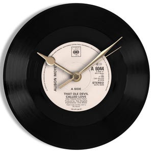 May include: A black vinyl record clock with gold-colored hands. The clock face is a record label with the text "THAT OLE DEVIL CALLED LOVE" and "ALISON MOYET". The clock is a unique decorative item.