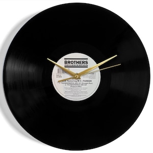 May include: Black vinyl record clock with gold hands. The record label features the text "Brothers Organisation" and "M.C. Parker" with the song title "Thunderbirds Are Go! (Straight Run)".