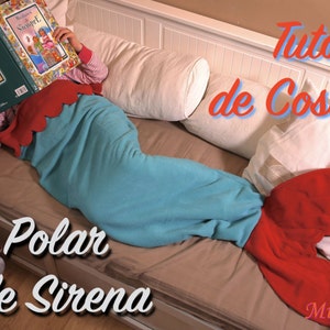 Puede incluir: Una manta de cola de sirena turquesa con una aleta roja. La manta está hecha de polar y es perfecta para acurrucarse en el sofá. El texto "Manta Polar Cola de Sirena" es visible en la imagen.