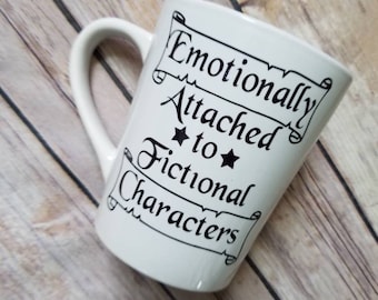 May include: White ceramic mug with a black design that reads "Emotionally Attached to Fictional Characters" in a scroll-like font.