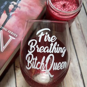 May include: A red glitter wine glass with the text "Fire Breathing Bitch Queen" in white lettering.