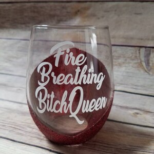 May include: A red glitter wine glass with the text "Fire Breathing Bitch Queen" etched on the side.