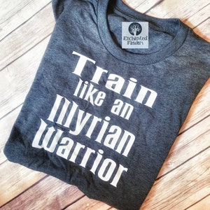 Puede incluir: Una camiseta gris oscura con texto blanco que dice "Train like an Illyrian warrior".