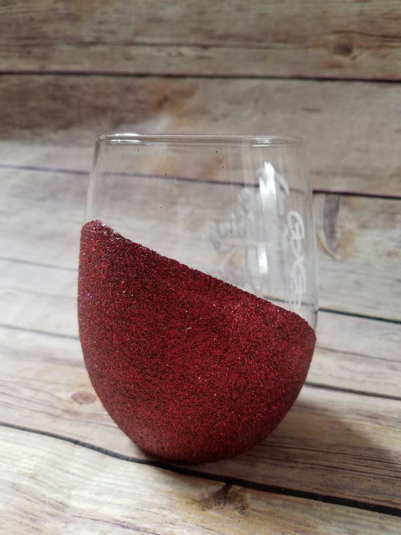 May include: A clear glass wine glass with a red glitter design on the bottom half. The glass has the text "It Goes" written on the side.