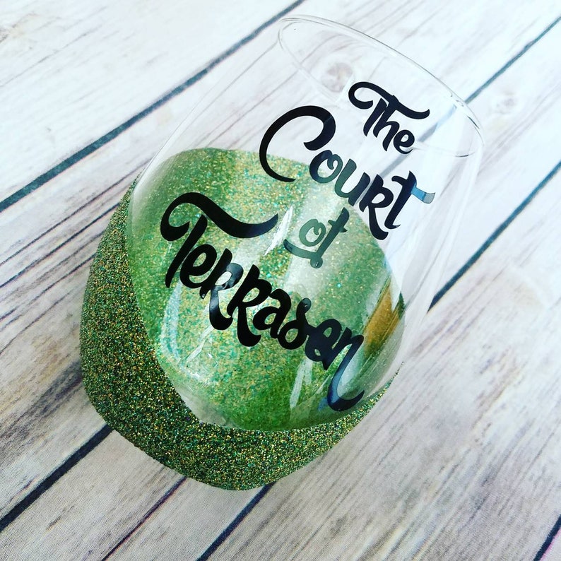 May include: A green glitter wine glass with the text "The Court of Terrasen" in black lettering.