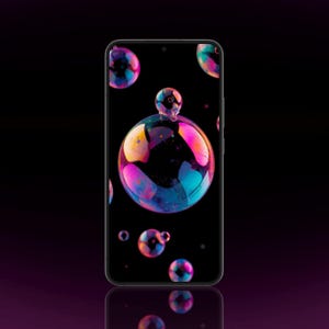 May include: A smartphone with a black frame and a dark screen displaying a vibrant wallpaper of iridescent soap bubbles in shades of pink, blue, and yellow against a deep black background. The device features a thin bezel and a front-facing camera.
