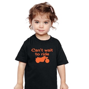 Könnte beinhalten: Ein schwarzes T-Shirt mit einer orangefarbenen Grafik eines Motorrads und dem Text "Can't wait to ride".