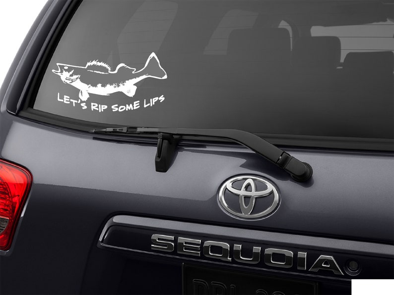 K&ouml;nnte beinhalten: Ein wei&szlig;er Vinyl-Aufkleber mit einer Silhouette eines Fisches und dem Text "Let's Rip Some Lips" auf einem grauen Auto.