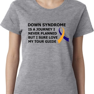 Op de afbeelding: Grijs T-shirt met een zwarte afbeelding met de tekst "Down Syndrome is a journey I never planned but I sure love my tour guide". Rechts van de tekst is een geel en blauw lint.