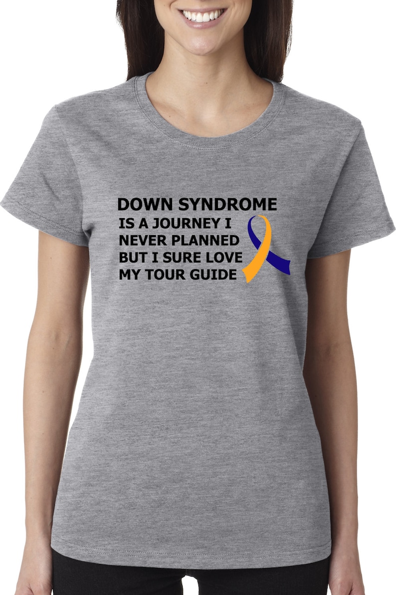 Op de afbeelding: Grijs T-shirt met een zwarte afbeelding met de tekst "Down Syndrome is a journey I never planned but I sure love my tour guide". Rechts van de tekst is een geel en blauw lint.