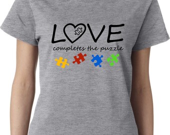 May include: Gray t-shirt with the text "LOVE completes the puzzle" in black. A heart with a puzzle piece inside is part of the word "LOVE". Four puzzle pieces in yellow, red, blue, and green are below the text.