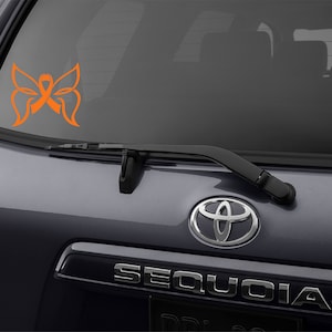 May include: A gray car with a rear window sticker of an orange butterfly with a ribbon in the center. The car has a chrome Toyota Sequoia emblem on the back.