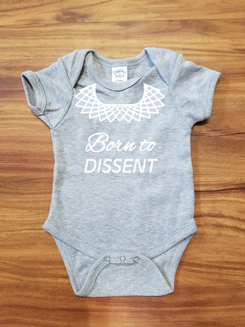 以下が含まれることがあります： 白い襟のデザインと「Born to Dissent」というテキストが書かれた灰色のベビーロンパースです。