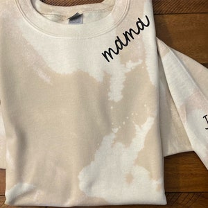 May include: A beige tie-dye sweatshirt with the word "mamma" on the front and "Jimmy Maggie" with a black heart on the sleeve.