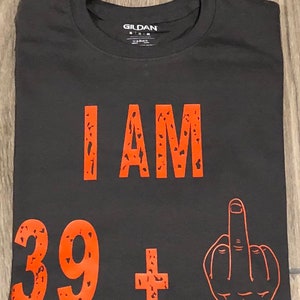 May include: Black t-shirt with the text "I AM 39+ " in orange with a middle finger graphic.