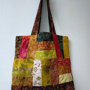 May include: A patchwork tote bag with brown, green, yellow, and red fabric squares. The bag has two brown straps.