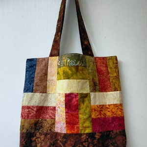 May include: A patchwork tote bag with a brown floral pattern on the bottom and a variety of colourful fabric squares in shades of red, orange, yellow, green, blue, and white.