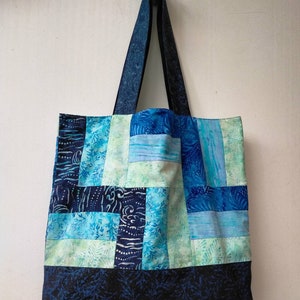 May include: A blue and green patchwork tote bag with a dark blue floral print on the bottom. The bag has two long straps.
