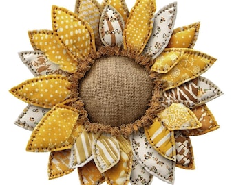 Könnte beinhalten: Eine handgefertigte Stoffsonnenblume mit einem Mittelteil aus Jute und genähten gelben und gemusterten Blütenblättern. Die Blütenblätter weisen verschiedene Designs auf, darunter Punkte, Streifen und Blumendrucke. Die Sonnenblume ist ein dekorativer Artikel.