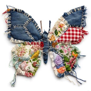 May include: A handcrafted butterfly decoration made from repurposed denim and fabric scraps. The wings feature patches of blue denim, floral prints, and red gingham, stitched together with white thread. The butterfly has a frayed edge and a whimsical, rustic aesthetic.