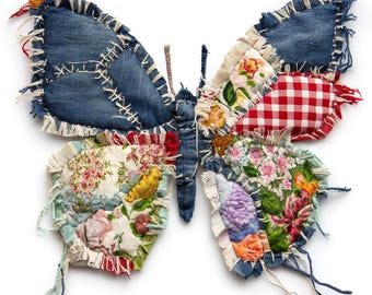 Könnte beinhalten: Ein handgefertigter Schmetterling aus recyceltem Jeansstoff und Stoffresten. Die Flügel zeigen Flicken aus blauem Denim, Blumenmustern und rotem Vichy, die mit weißem Faden zusammengenäht sind. Der Schmetterling hat einen ausgefransten Rand und einen rustikalen Look.