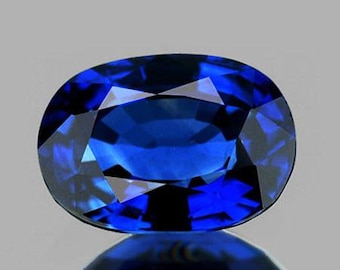 Könnte beinhalten: Ein facettierter, oval geschliffener Saphir. Der Edelstein hat eine tiefe, lebendige blaue Farbe mit inneren Reflexionen. Der Saphir liegt vor einem hellgrauen Hintergrund und spiegelt sich.