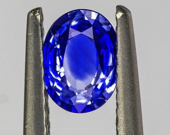 Könnte beinhalten: Ein leuchtend blauer ovaler Saphir-Edelstein, der in einer Metallzange gehalten wird.