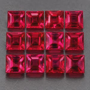Puede incluir: Un conjunto de doce piedras preciosas de color rojo vibrante, talladas en forma cuadrada y dispuestas en una cuadrícula de tres filas y cuatro columnas. Cada piedra presenta una superficie facetada que refleja la luz, creando un patrón simétrico.