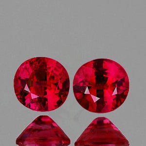 Puede incluir: Dos gemas redondas, facetadas, de color rojo intenso, con talla brillante. Las gemas se muestran con sus reflejos, mostrando sus superficies pulidas y facetas internas. Las piedras son de un tono rojo vibrante.