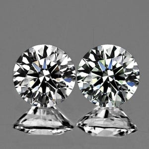 May include: Two round-cut, brilliant-faceted diamonds. The diamonds are clear and sparkling, with multiple facets reflecting light. Each diamond sits atop a small, clear, diamond-shaped base, creating a mirrored effect against a gray background.