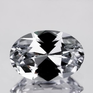 May include: A clear oval-shaped gemstone with a faceted cut. The gemstone is reflecting light, creating a sparkling effect.