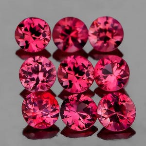 Puede incluir: Nueve gemas redondas, facetadas, de color rosa intenso están dispuestas en una cuadrícula. Las gemas tienen un alto grado de claridad y brillo, reflejando la luz. Las gemas están sobre una superficie oscura y reflectante.