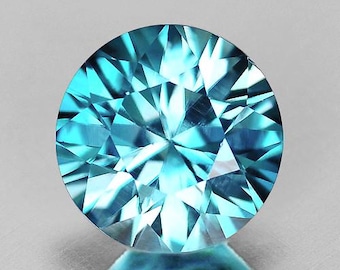 Puede incluir: Una gema redonda y facetada con talla brillante. La gema es de un color turquesa vibrante, con múltiples facetas que reflejan la luz. La piedra preciosa se encuentra sobre un fondo neutro, resaltando su claridad y brillo. La forma de la gema es perfectamente circular.