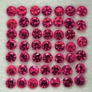 Pode incluir: Uma coleção de pedras preciosas redondas, facetadas, rosa escuro, dispostas em um padrão de grade. As gemas têm um corte brilhante, refletindo a luz e mostrando sua estrutura interna. As pedras estão sobre um fundo claro e texturizado.