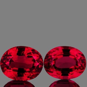 May include: Two oval-shaped, deep red gemstones with a faceted cut.