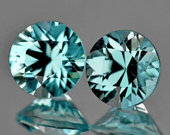 Puede incluir: Dos piedras preciosas redondas y facetadas de color azul verdoso. Las piedras preciosas tienen un patrón de estrella en el centro.