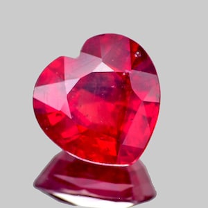 Puede incluir: Una piedra preciosa de rubí en forma de corazón con un color rojo intenso. La piedra preciosa está tallada y pulida, con facetas que reflejan la luz.