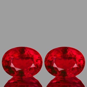May include: Two oval-shaped, deep red gemstones. The gemstones are faceted and have a high polish.
