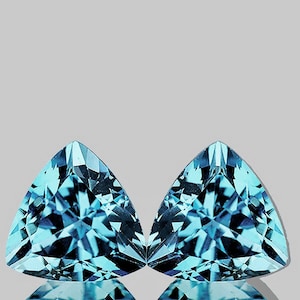 May include: Two triangular blue topaz gemstones with a faceted cut. The gemstones are set against a white background.