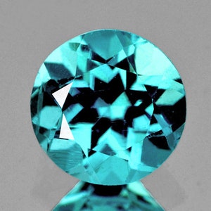 May include: A round, faceted gemstone with a blue-green color. The gem has a star-like pattern inside.