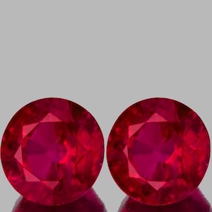 Puede incluir: Dos piedras preciosas de rubí redondas y facetadas de color rojo intenso. Las piedras preciosas están engastadas en una superficie pulida y reflectante.