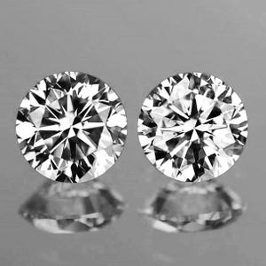 May include: Two round-cut diamonds with brilliant facets, reflecting light and creating a sparkling effect. The diamonds are set against a gray background, with their reflections visible below. The image showcases the clarity and brilliance of the gemstones.