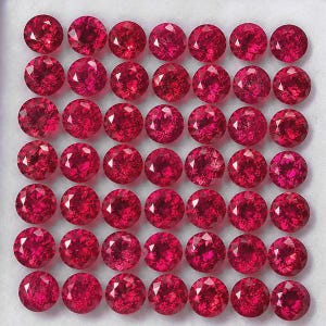 Può includere: Una collezione di quarantanove pietre preziose rosse rotonde e sfaccettate disposte in una griglia di sette per sette. Ogni pietra presenta un taglio brillante con molteplici superfici riflettenti, mostrando un colore rosso intenso e vivace.