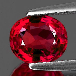 Puede incluir: Una piedra preciosa de rubí ovalada de color rojo intenso, sostenida por unas pinzas.