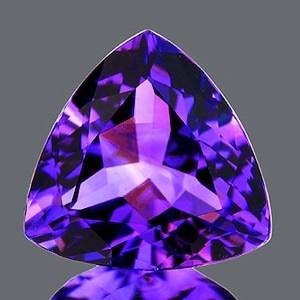 Puede incluir: Una gema facetada de forma triangular con un tono púrpura intenso. La superficie de la gema refleja la luz, mostrando una compleja estructura interna. El corte de la piedra crea múltiples facetas, realzando su brillo y color.