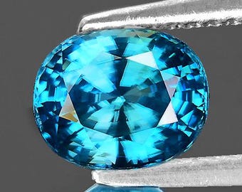 Könnte beinhalten: Ein leuchtend blauer ovaler Edelstein mit facettiertem Schliff. Der Edelstein wird von einer Pinzette gehalten.